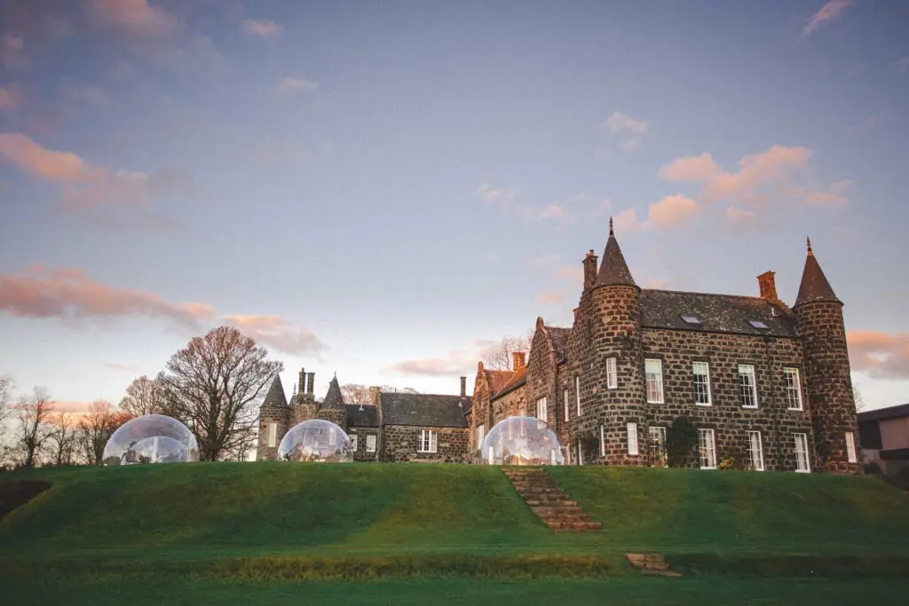 Meldrum House, a stone manor house with round towers and glass dining domes on the lawn at sunset, Oldmeldrum, Aberdeenshire